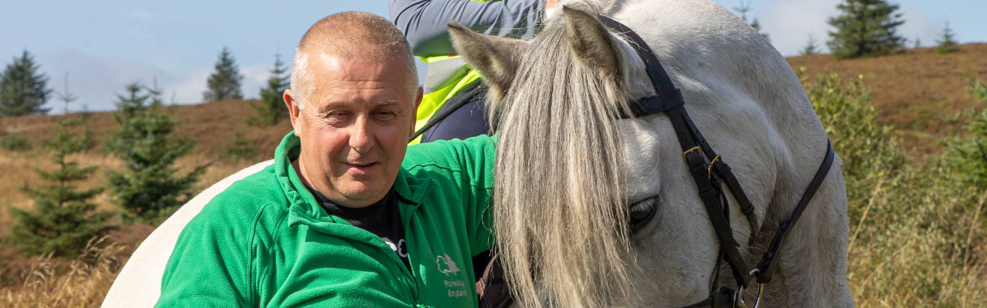 A Forestry England representative stands beside a horse in Kielder Forest, highlighting the strong connection between Northumberland's forests and equestrian access celebrated during the 100 Years of Kielder Forest programme.